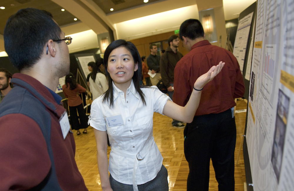 A student actively presenting her research poster to a fellow student.